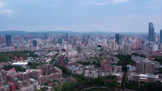 A wide aerial view of a sprawling urban area with mixed buildings, green spaces, and distant hills under a clear daytime sky.