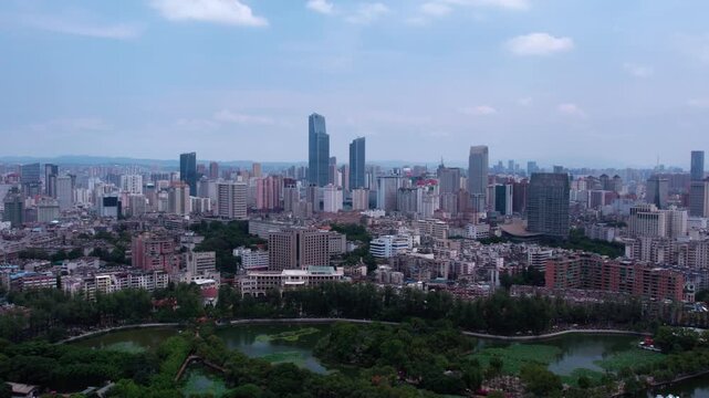 A wide aerial panorama of a sprawling urban city with high-rise buildings, a green lake, and trees under a clear sky.