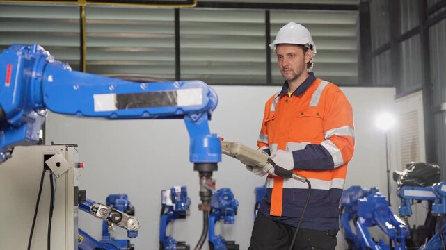 Robotic engineer holding controller programming industrial robot arm in factory, automation technician operating smart factory robotic machinery with pendant, engineer testing robotic arm in plant
