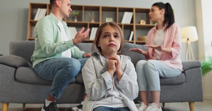 Child watches parents argument at home in fear. Upset child sits near sofa as parents argue, showing family conflict and stress in domestic life. Clear family conflict and stress concept.