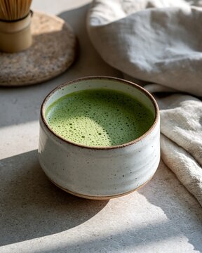 Ceramic cup filled with foamy green matcha tea on a rustic stone table