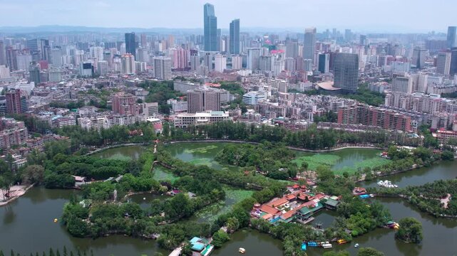 An aerial panorama shows a city with dense buildings and a large green park containing lakes and trees.