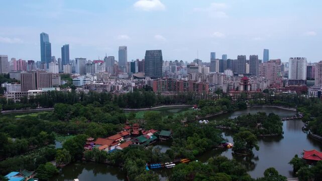 A panoramic daytime view of a modern city, featuring dense urban buildings and a large green park with lakes in the foreground.