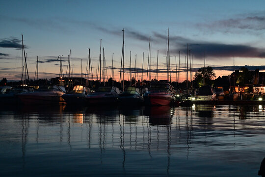 Boats Docked at Marina During Sunset Dusk With Reflective Water and Harbor Lights - the summer landscape of Mikołajki in Masuria.