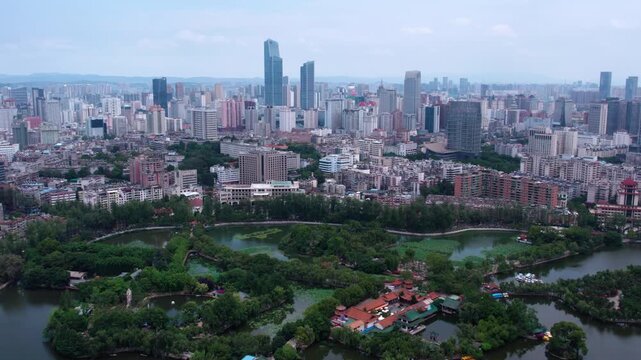 A high-angle aerial panorama showing a modern urban city with dense buildings, a central park with lakes and greenery.