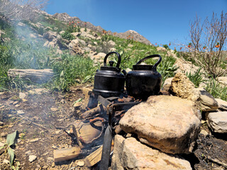 Two blackened kettles rest over burning wood, smoke drifting past wild Crown Imperial blooms scattered across a rugged mountainside. 📍 Ghallakhane, Daraki, Kurdistan  © Hawraman83
