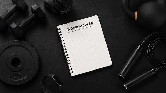 Flat lay top view of blank workout plan notebook surrounded by dumbbells kettlebell jump rope and fitness accessories on dark background
