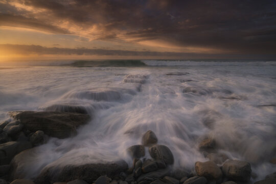 peaceful sunset ocean landscape with long exposure water waves over rocks creating a calm and serene atmosphere in azkorri beach