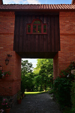 A brick arch with a red wooden window with a passage underneath and a view of the lush garden path.