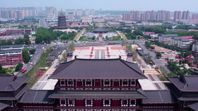 An aerial view of a traditional Chinese architectural complex with a large square, adjacent to modern urban cityscape on a clear day.