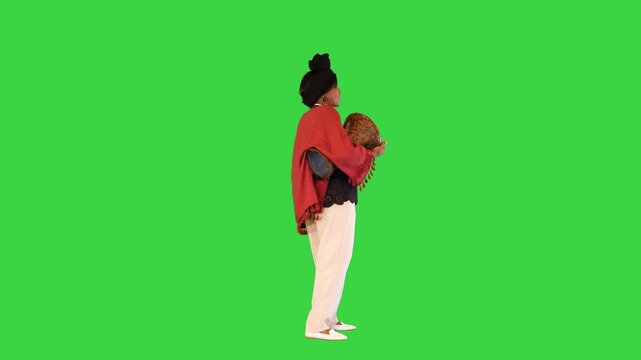 Cheerful african american woman in traditional clothes beats djembe drum and dances on a Green Screen, Chroma Key.