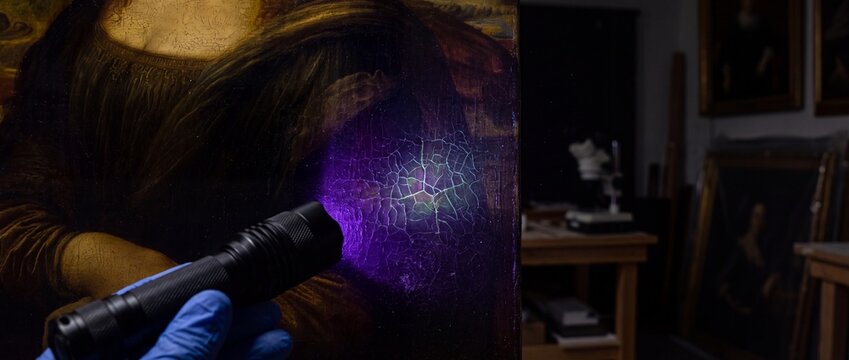 Art conservator examining renaissance painting detail with uv light revealing craquelure texture and restoration needs