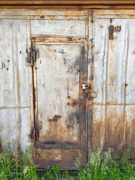 Rusty metal garage door with iron gate and padlock on corroded abandoned warehouse exterior wall
