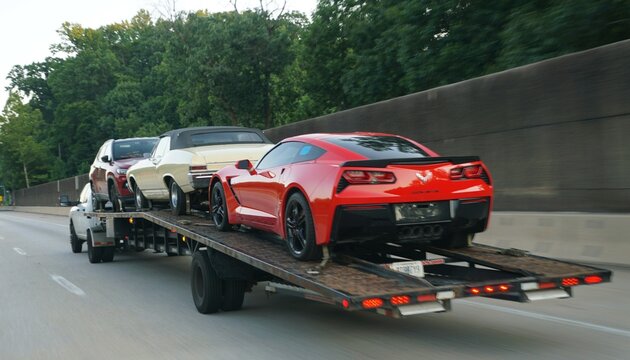 Pennsylvania, U.S.A - Jul 11, 2026 - A flatbed truck carrying three vehicles, including a red Chevrolet Corvette, classic convertible, and SUV on the highway.