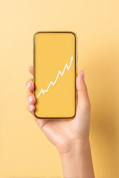 Person holding a mobile device showing a chart on a bright yellow backdrop for promotional and stock photography purposes