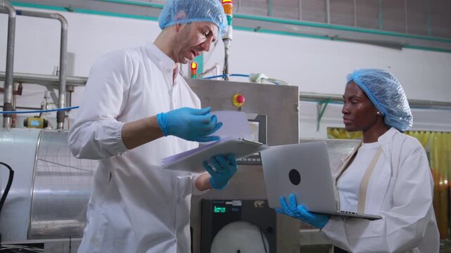 Two engineer inspect heavy machine in juice bottling factory using laptop and document on clipboard, Industrial food production plant, inspection and maintenance while recording data on laptop.