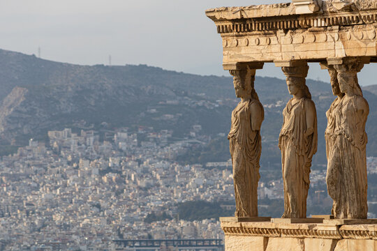 The majestic Caryatids statues of the Porch of the Maidens on the Erechtheion at the Acropolis, Athens, with the sprawling cityscape and mountains behind.