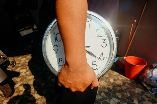close-up shot of a person carrying a large round wall clock under their arm outdoors.