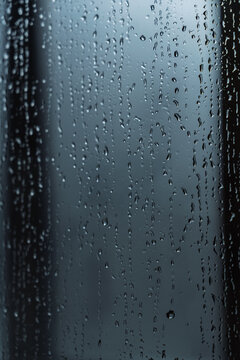 Raindrops on a window pane with a dark moody background
