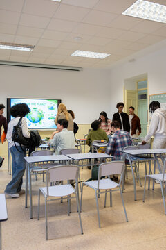 Diverse high school students entering a classroom with an interactive screen displaying an environmental concept