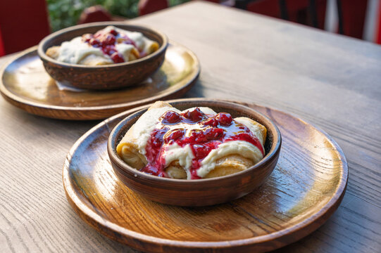 Two bowls of delicious crepes with sweet cream and cherry sauce on a wooden table