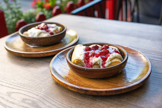 Two bowls of delicious crepes with sour cream and cherry jam on a wooden table