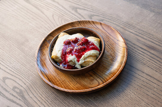 Delicious crepes with cream and cherry sauce on a wooden plate