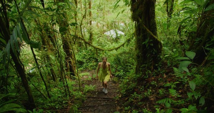 Woman walks up a wooden and earth staircase through incredibly dense Costa Rican rainforest wilderness