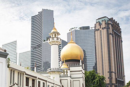 The golden dome and minaret of Sultan Mosque in Kampong Glam rise in contrast against modern glass skyscrapers in the Singapore skyline