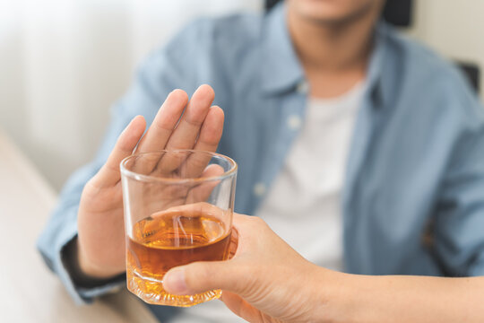 Alcoholism, depressed asian young man refuse, push out alcoholic beverage glass, drink whiskey, sitting alone at night. Treatment of alcohol addiction, having suffer abuse problem alcoholism concept.