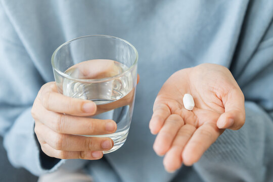 Sick, asian young woman, girl hand holding pill, painkiller medicine from stomach pain, headache, pain for treatment, take drug or vitamin and glass of water at home, pharmacy and health care concept.