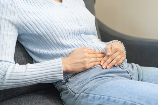 Sick asian young woman in pain, hand holding belly, lying on the sofa with a stomachache, hurt abdomen ache and digestive problem, gastritis or diarrhea. Health care inflammation, abdominal problem