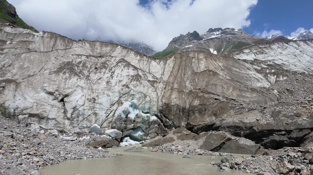 Rugged terrain of the Shkhara glacier in Svaneti Georgia, featuring massive ice walls covered in dirt and rocky debris, melting glacier creating a muddy stream, perfect for adventure travel, global