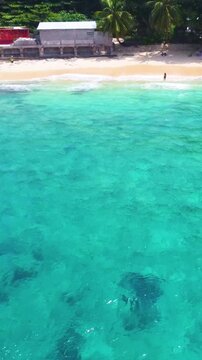 Vertical aerial pull back view revealing Glacis Beach in Seychelles with turquoise water, white sand, granite rocks and lush tropical coastline.