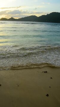 Vertical panoramic view of sunset at Baie Lazare beach on Mahe Island in Seychelles with golden light, calm ocean and tropical coastal scenery.