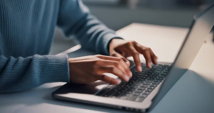Person wearing blue sweater typing on laptop keyboard at office desk