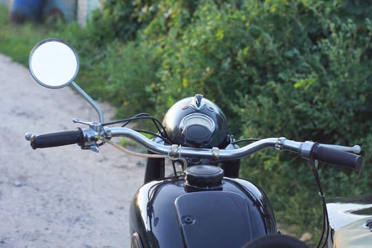 one small old round rearview mirror on the handlebars of an old black retro motorcycle on a daytime summer street