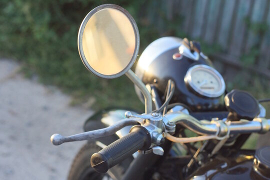 one small old round rearview mirror on the handlebars of an old black retro motorcycle on a daytime summer street
