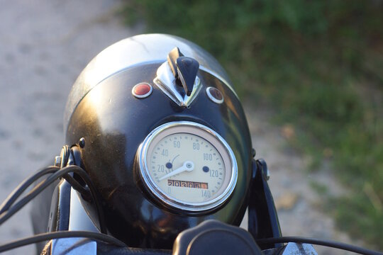 A one old round gray retro speedometer on an old black motorcycle on a street a summer day in the street