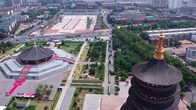 High-angle aerial view of ancient pagoda and traditional buildings amidst modern urban landscape with green spaces and roads.