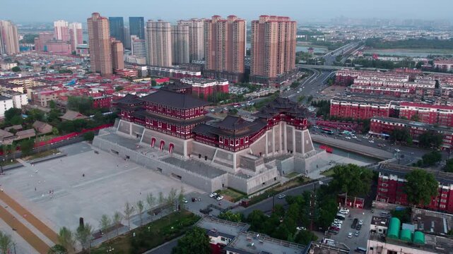 Aerial shot of a grand traditional Chinese building set within a modern urban cityscape with high-rise residential structures nearby.