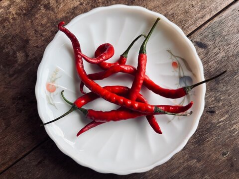 Fresh red chili peppers arranged on a white floral plate over a rustic wooden table, showcasing vibrant color, natural texture, spicy ingredient, and traditional culinary appeal. for cooking