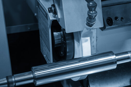 Surface finishing process on metal shaft part using cylindrical grinding machine in blue tone lighting