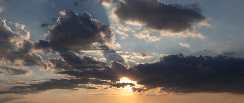 Panoramic sky with sun rays breaking through clouds at sunset