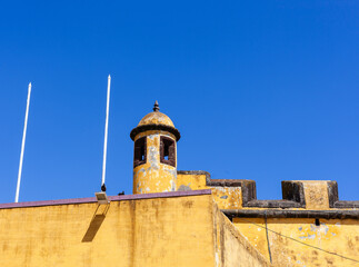 Obraz premium Historic stone fortress tower under clear blue sky. Forte de Sao Tiago in Funchal, Madeira. Coastal military architecture with watchtower and battlements.