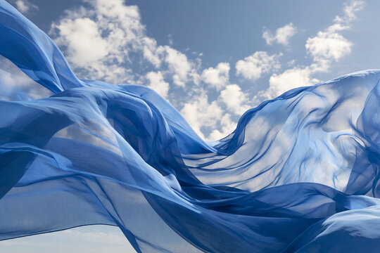 Flowing blue fabric billows gracefully against a partly cloudy sky. Elegant textile concept for fashion and freedom banners.