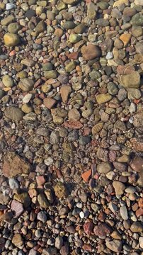 Clear shallow sea water ripples gently over colorful pebbles and stones on the seabed