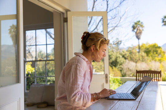 young woman typing on laptop under patio, palm trees in background