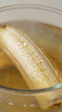 Ripe banana simmering in clear glass bowl of hot water
