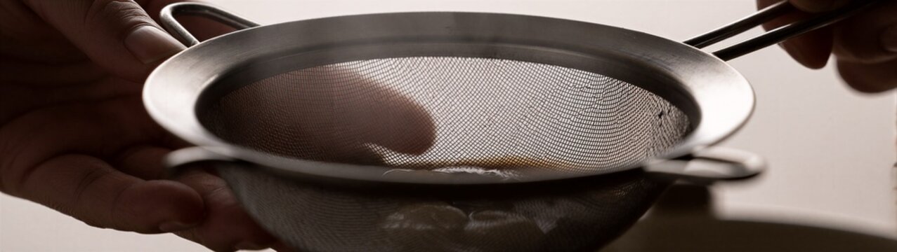 Hands sifting batter through fine mesh strainer in kitchen